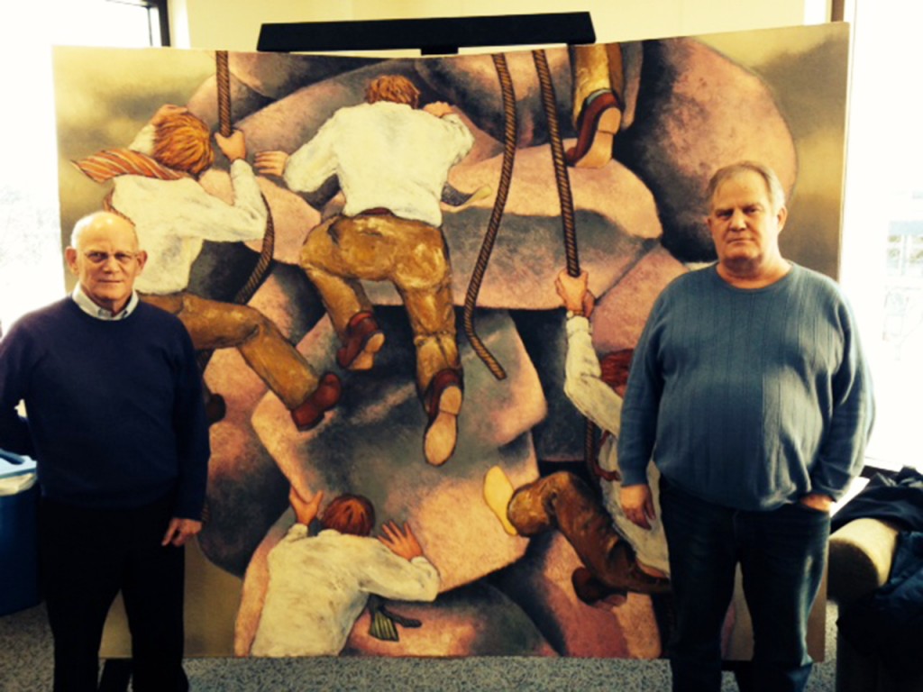 Cobber alums and brothers Mark Budd (left) and Eric Budd (right) stand in front of Eric’s painting “The Rock Climbers.” Mark donated the painting to the college after he returned to Concordia last spring and saw the art lining the walls of the Offutt School of Business. Submitted photo.