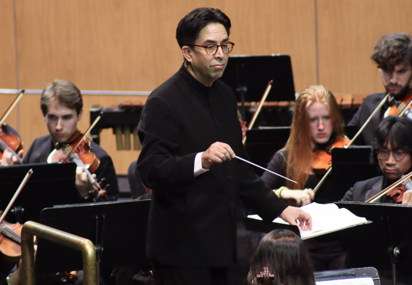 A man with a conducting baton stands in front of an orchestra